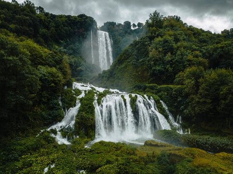 Aerial view of the majestic Marmore Falls cascading through lush green forest and serene river, Terni, Italy.