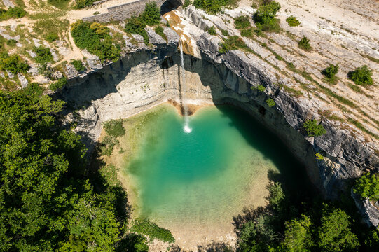 Aerial view of a breathtaking waterfall cascading into a turquoise pool surrounded by lush green forest and rocky cliffs, Pican, Croatia.