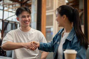 A handsome, cheerful Asian man is shaking hands with his female colleague.