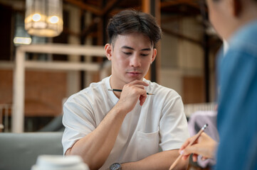 A serious, thoughtful Asian man listening to his friend's ideas during the meeting at a coffee shop.
