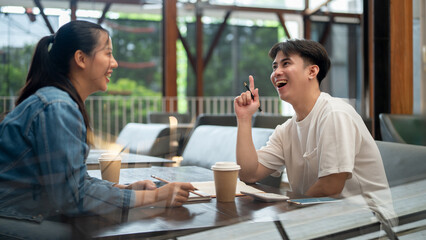 Two cheerful young Asian college students enjoying discussing work together at a coffee shop.