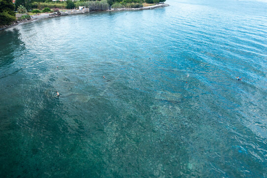 Aerial view of tranquil azure coastline with crystal clear water and serene reflections, Archea Epidavros, Greece.
