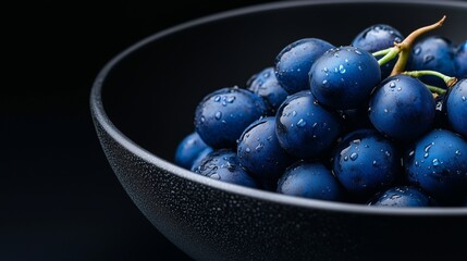 Fototapeta premium Vibrant blue grapes glisten in a sleek black bowl, showcasing elegance and beauty against a dark backdrop.