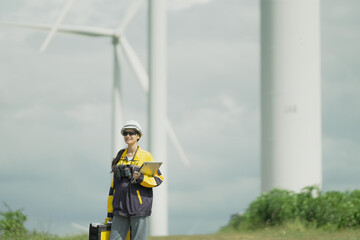 A female engineer in a hardhat stands in front of a field of wind turbines at sunset.