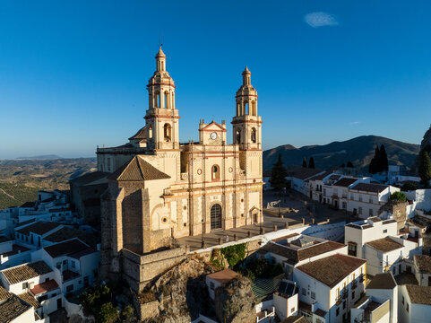 Aerial view of picturesque old town with whitewashed rooftops and historic church surrounded by mountains, Olvera, Spain.