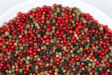 A mixture of different peppercorns on a white background, top view