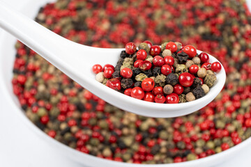 Different varieties of peppercorns, red, green, black and white peppers in a spoon