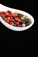 Different varieties of peppercorns, red, green, black and white peppers in a spoon