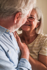 Portrait of a mature couple embracing each other in their home, posing affectionately for a photo in front of the camera. They share a loving glance after a lifetime together, smiling in casual