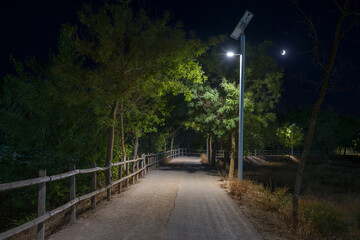 A solar-powered streetlight stands tall at night along a tranquil park path, the solar panels are...