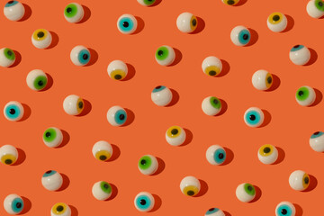 Creative pattern made of gummy candies in eyeball shape, an orange background. Spooky Halloween idea. Minimal concept.