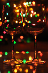Two transparent wine glasses filled with water, with colorful Christmas lights on a tree in the background