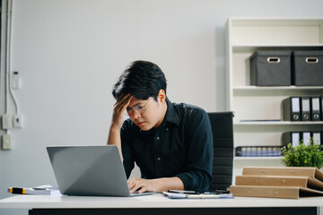 Frustrated young businessman working on a laptop computer sitting at his working place