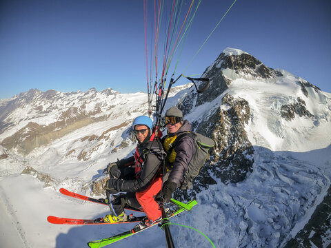 Two paragliders soar above snowy mountains with skis