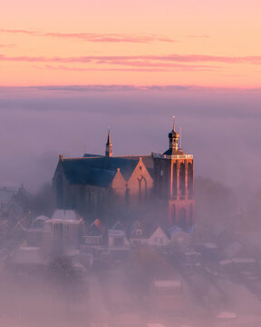 Aerial view of a foggy cityscape at sunrise featuring a historic church, Workum, Friesland, Netherlands.