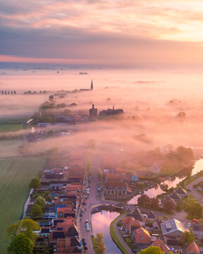 Aerial view of a tranquil city with fog and low clouds at sunrise, featuring a charming church and canal, Workum, Friesland, Netherlands.
