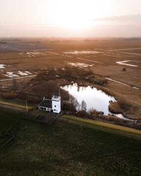 Aerial view of a beautiful lighthouse at sunrise beside a tranquil lake and serene countryside fields, Workum, Netherlands.