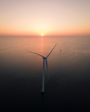 Aerial view of wind turbines at sunrise over the serene sea, Ijsselmeer, Netherlands.