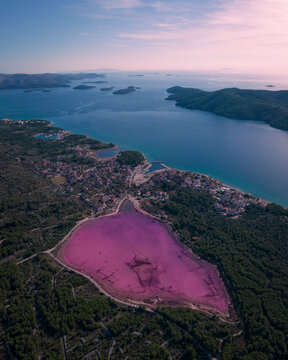 Aerial view of a pink lake surrounded by a scenic town and coastline, Zablace, Croatia.