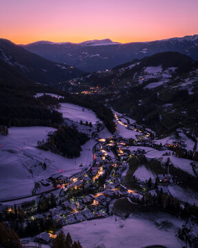 Aerial view of a beautiful village in a snow-covered valley surrounded by majestic dolomites at sunset, Santa Magdalena, Italy.