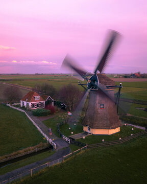 Aerial view of a picturesque windmill surrounded by tranquil fields under a pink sky at sunrise, Workum, Netherlands.