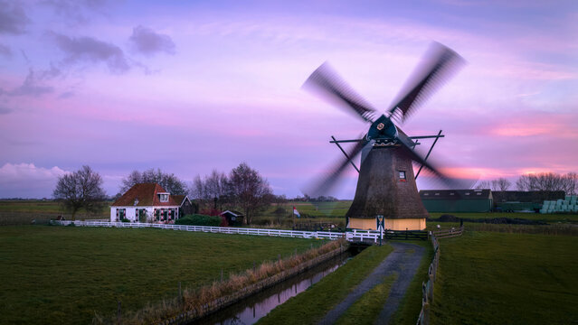 Aerial view of a beautiful traditional windmill at sunrise surrounded by serene fields and a tranquil canal, Workum, Netherlands.