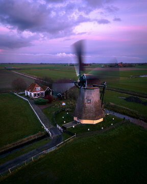 Aerial view of traditional windmill at sunrise with scenic countryside fields and tranquil sky, Workum, Netherlands.