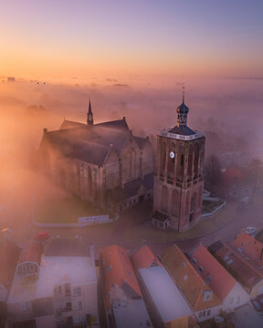 Aerial view of a tranquil city shrouded in fog at sunrise with a historic church, Workum, Friesland, Netherlands.