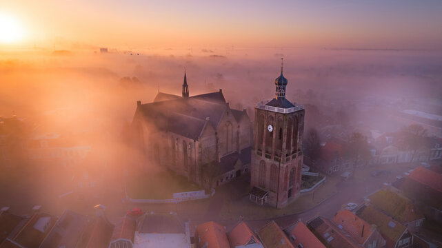 Aerial view of a historic city with a beautiful church shrouded in fog and low clouds at sunrise, Workum, Netherlands.