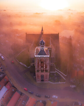 Aerial view of a beautiful city enveloped in fog at sunrise with a historic church, Workum, Netherlands.