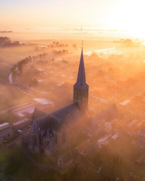 Aerial view of a tranquil city shrouded in fog at sunrise with a historic church steeple, Workum, Netherlands.