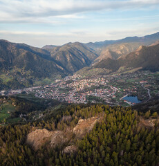 Obraz premium A spring mountain valley at sunrise with rich vegetation and spruce dark dense forests and a small picturesque town of Smolyan nestled between the slopes, Rhodopi Mountains, Bulgaria.