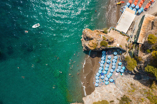 Aerial view of the picturesque beach with umbrellas and boats by the turquoise sea, Positano, Italy.