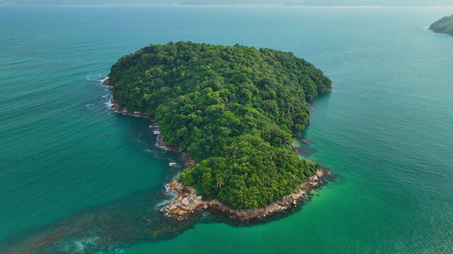 Aerial view of a lush tropical island surrounded by serene ocean and vibrant coastline, Ubatuba, Brazil.