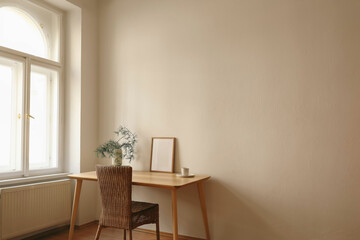 Christmas Scandinavian interior. Minimal winter home decor composition. Blank vertical wooden picture frame mockup, cup of coffee. Table near window. Pine tree branches, vase. Beige wall background