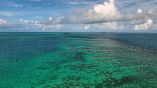 Aerial view of serene turquoise reef and clear water under a sunny blue sky, Manuka, Tonga.