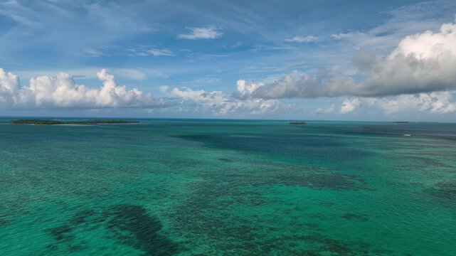 Aerial view of tranquil ocean and pristine reef under a clear blue sky with clouds, Manuka, Tonga.