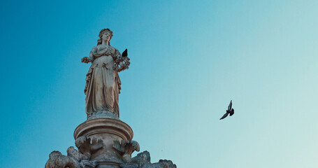 Mumbai, India. Pigeon Sits On Flora Fountain. Fly Of Pigeons Above Flora Fountain. Fountain Located At Hutatma Chowk Is Ornamentally Sculpted Architectural Heritage Monument. Located At Southern End