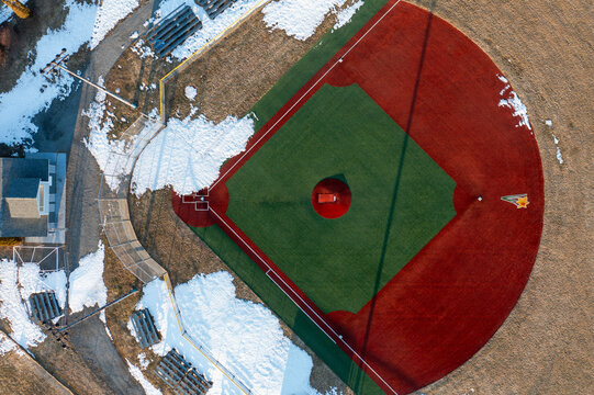 Aerial view of a snow-covered baseball field surrounded by urban buildings and bleachers, Sydney City, Canada.