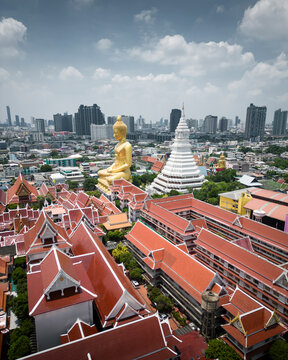 Aerial view of a vibrant cityscape featuring a majestic buddhist temple and golden statue under a cloudy sky, Phasi Charoen, Thailand.