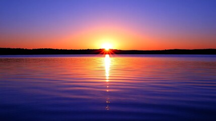 Fototapeta premium A beautiful sunrise over a still lake with a bright orange sun reflecting on the water.