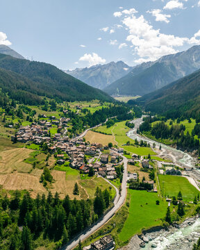 Aerial view of a picturesque village nestled in a lush valley with a serene river and vibrant mountains, Cogne, Italy.