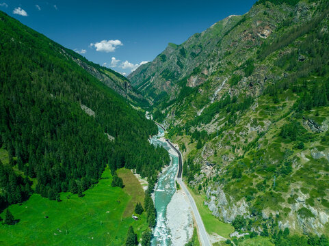 Aerial view of majestic alps with a serene river and winding road through a picturesque valley, Cogne, Italy.