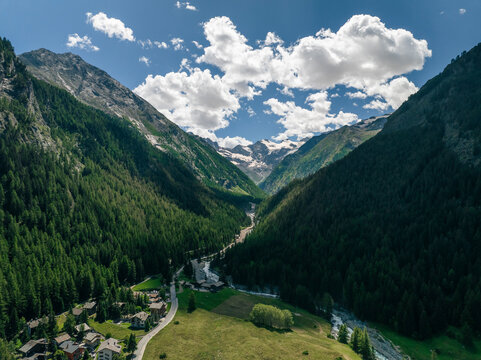 Aerial view of lush valley with serene river and picturesque village surrounded by majestic mountains and forest, Gran Paradiso National Park, Cogne, Italy.