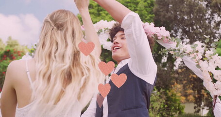 Image of pink hearts over happy diverse couple dancing in garden on wedding day