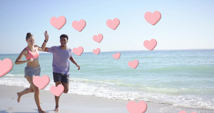 Image of pink hearts over diverse couple running on beach