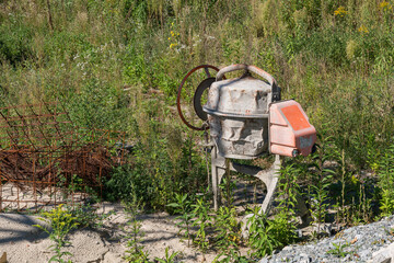 Abandoned cement mixer in overgrown construction site during summer
