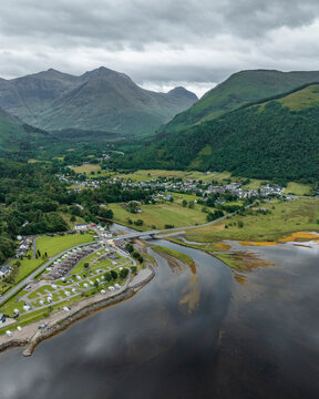 Aerial view of loch leven surrounded by beautiful mountains and a quaint village, Glencoe, United Kingdom.