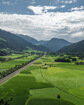 Aerial view of lush green fields and majestic mountains in a tranquil valley, Freienfeld, Italy.