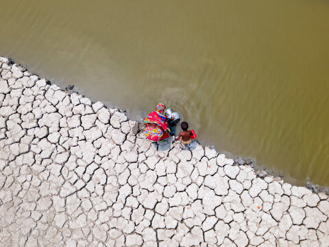 Aerial view of a coastal village facing drought with cracked earth and a community collecting water, Khulna, Bangladesh.